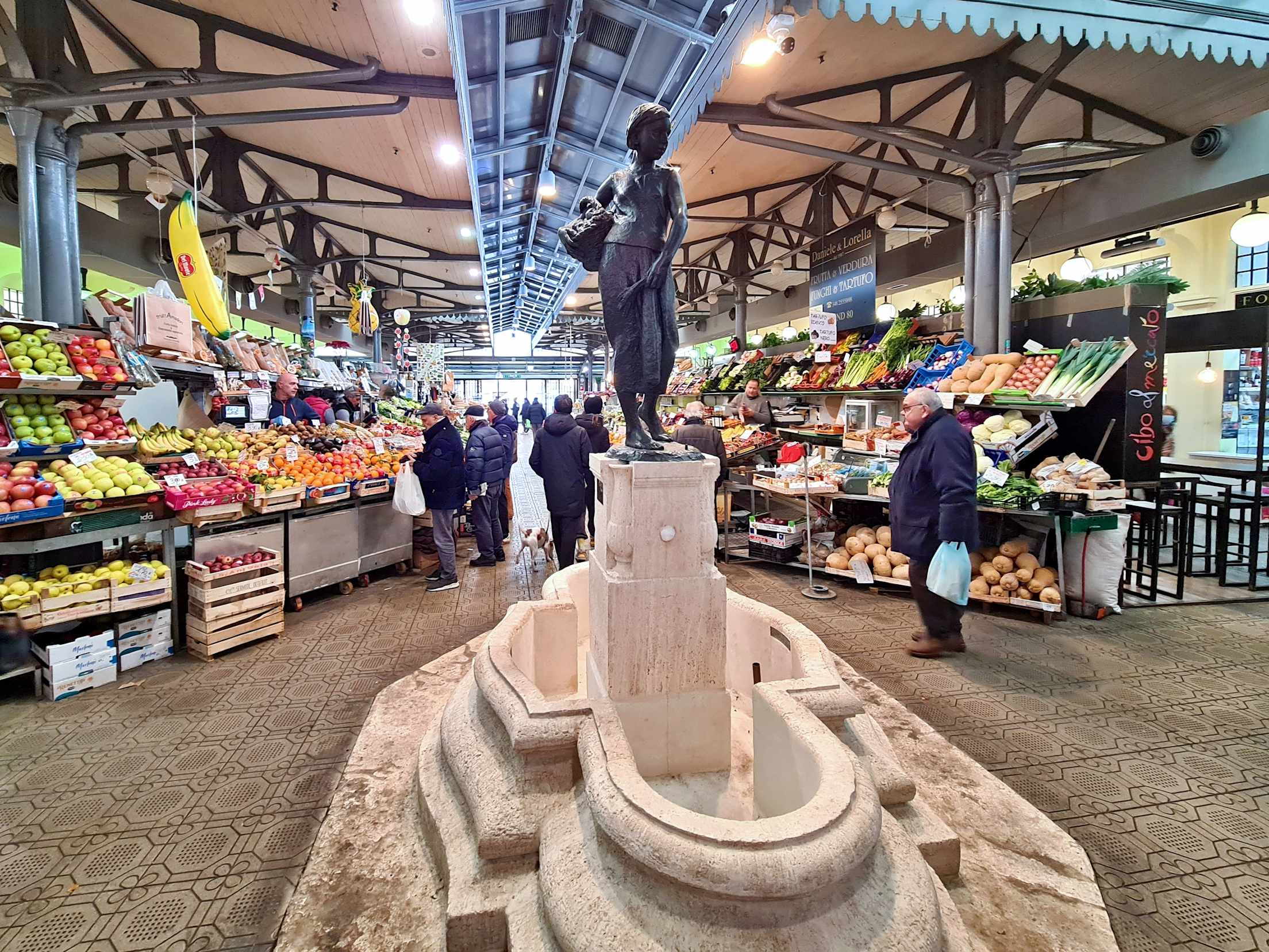 A statue of a woman at the center of a produce market. 