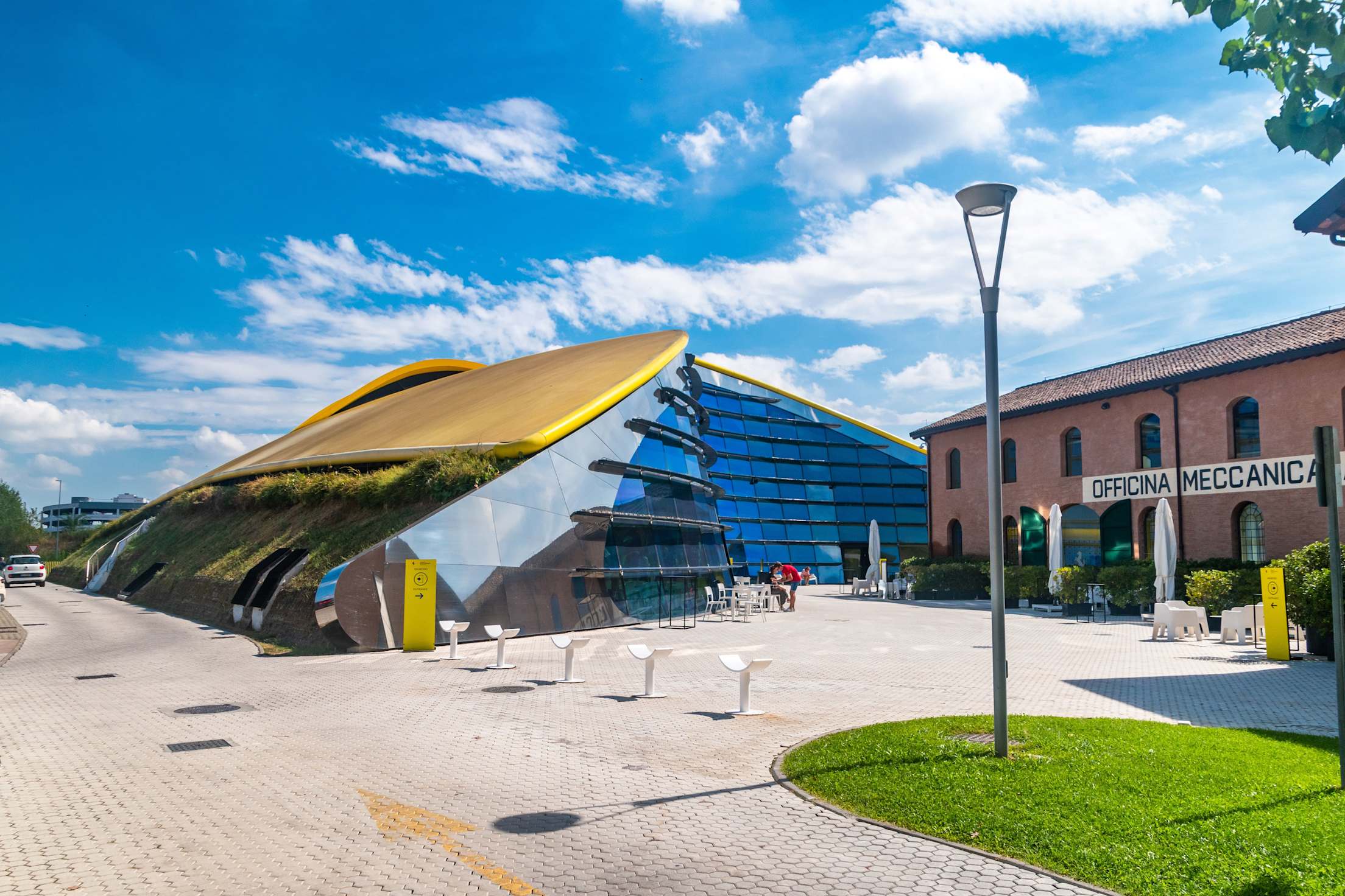 The Enzo Ferrari Museum—a sleek, yellow, wave-shaped pavilion juxtaposed next to a brick building.