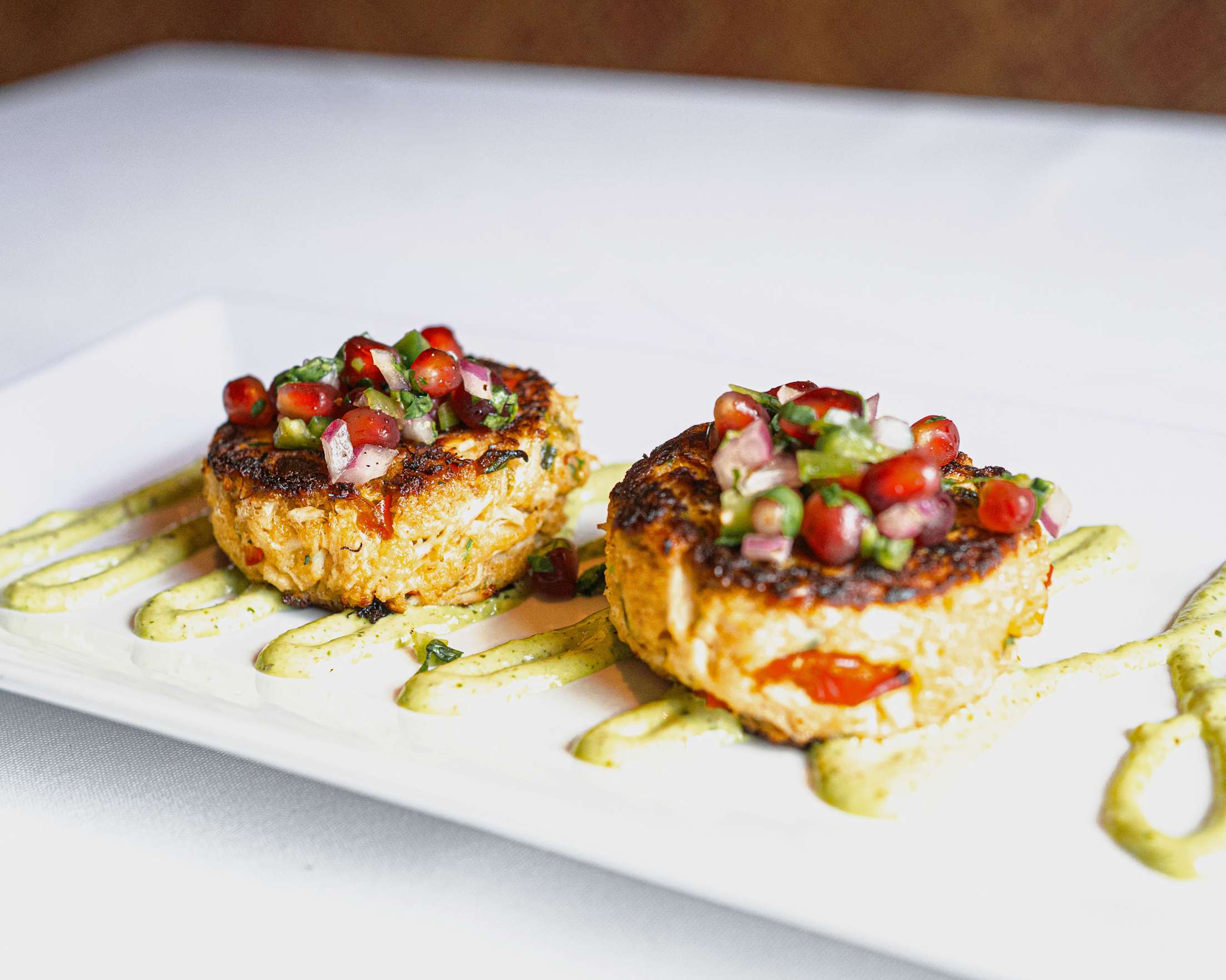 Crab cakes topped with colorful salsa sit atop a green sauce