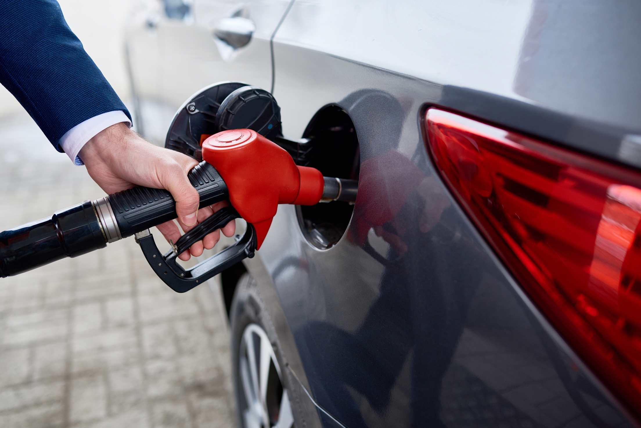A red gas pump nozzle filling a sedan.