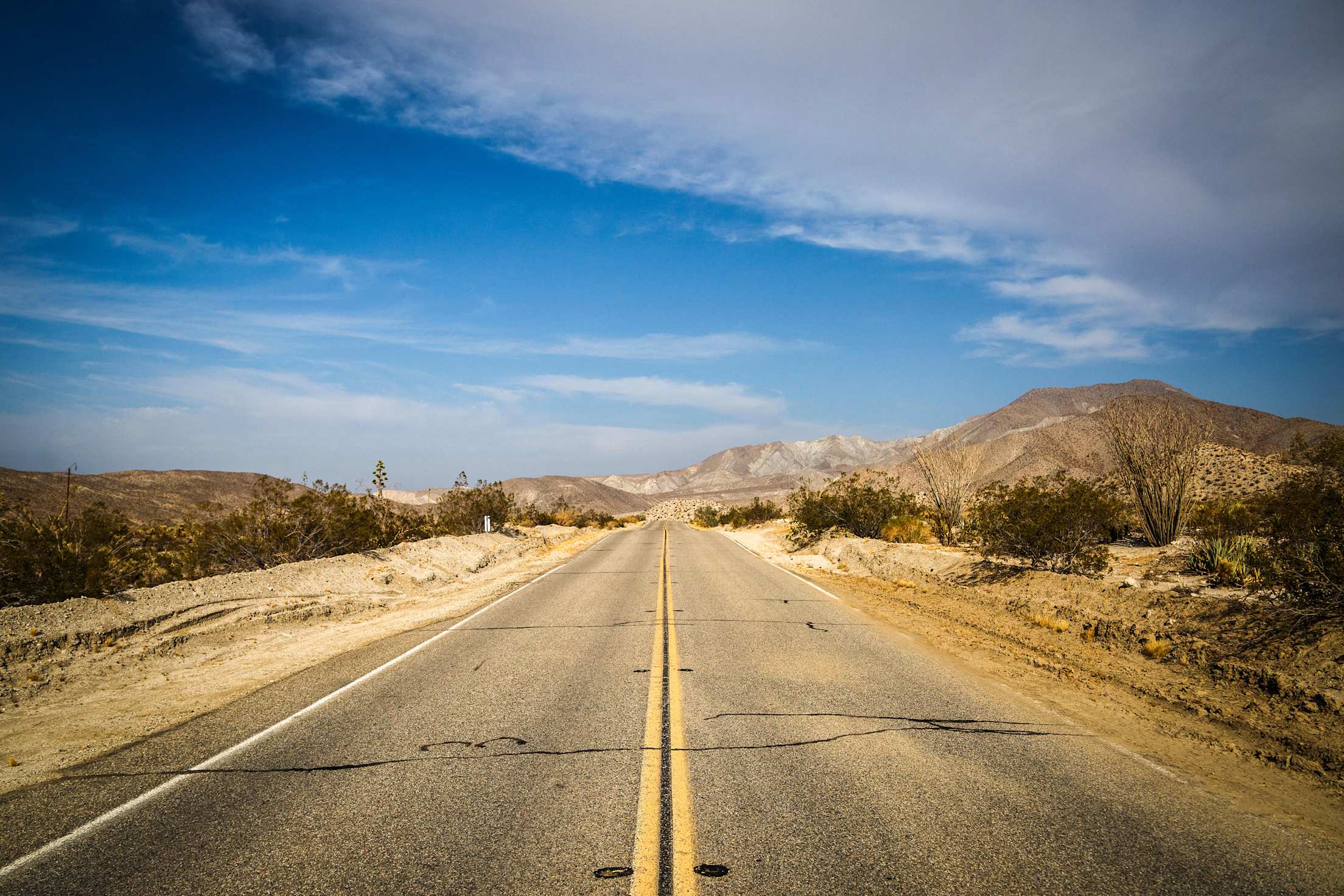 a dusty desert highway with blue sky and mountains in the distance