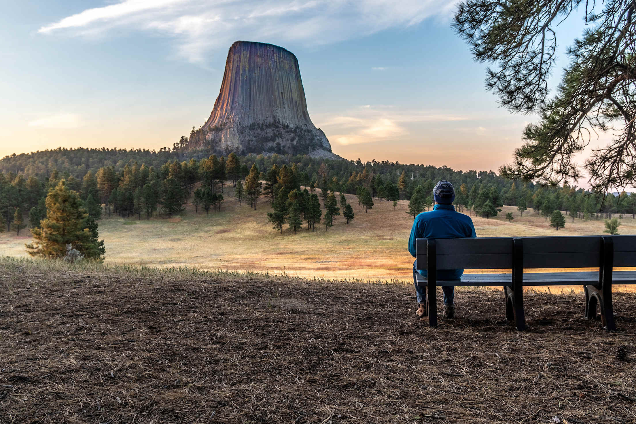 a man sits on a bench facing a dramatic tower monument