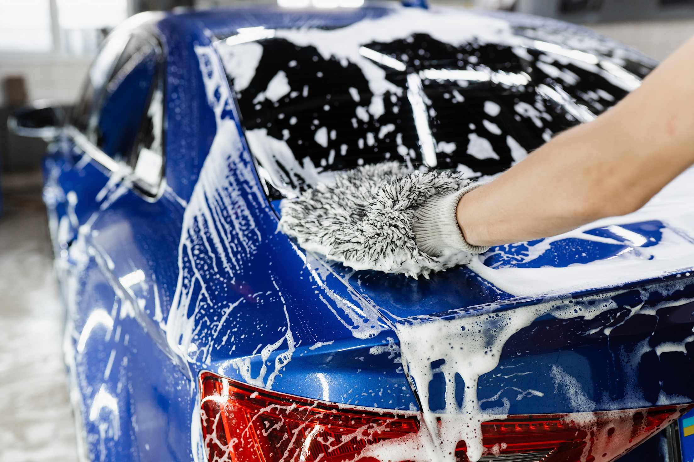 A person cleans their car with a soft mitt and soapy water.