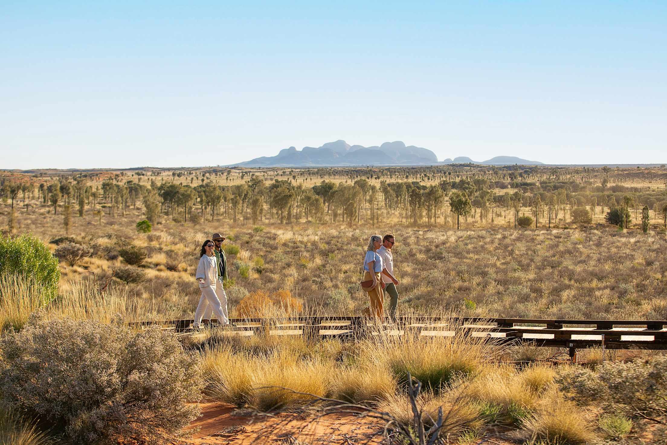 people walk through dry grass and a scenic plain with mountains in the background
