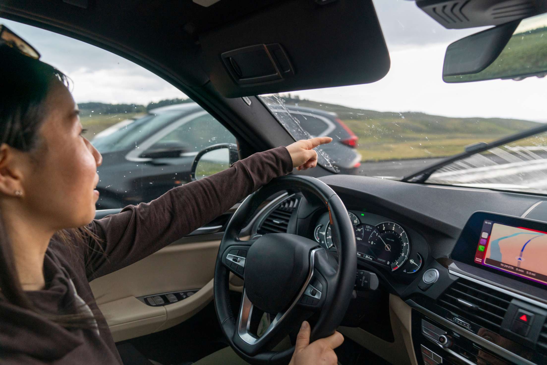 A woman points out of her car windshield as rain begins to fall.