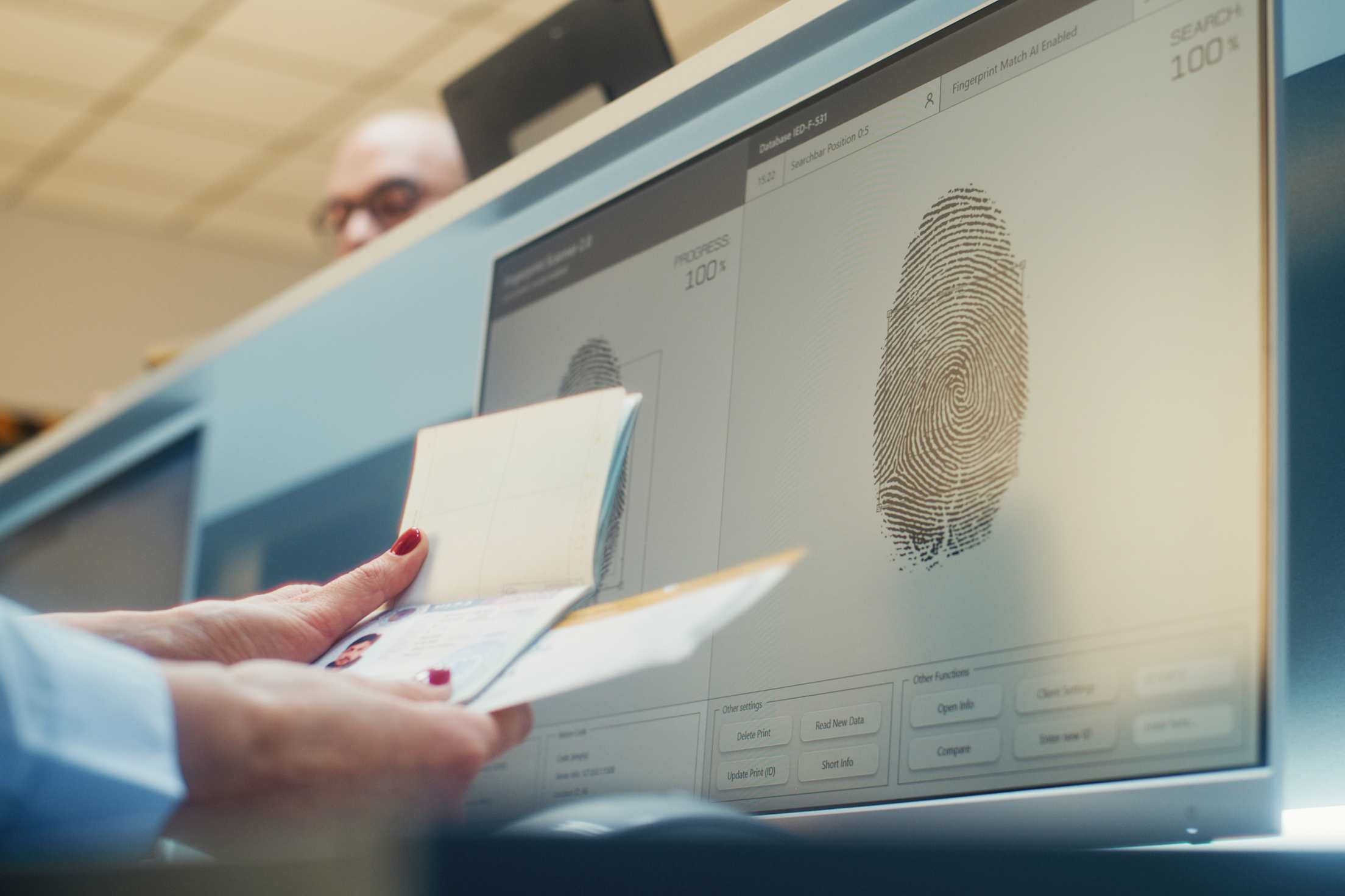 An airport security officier reviews a passport and a fingerprint on a computer.