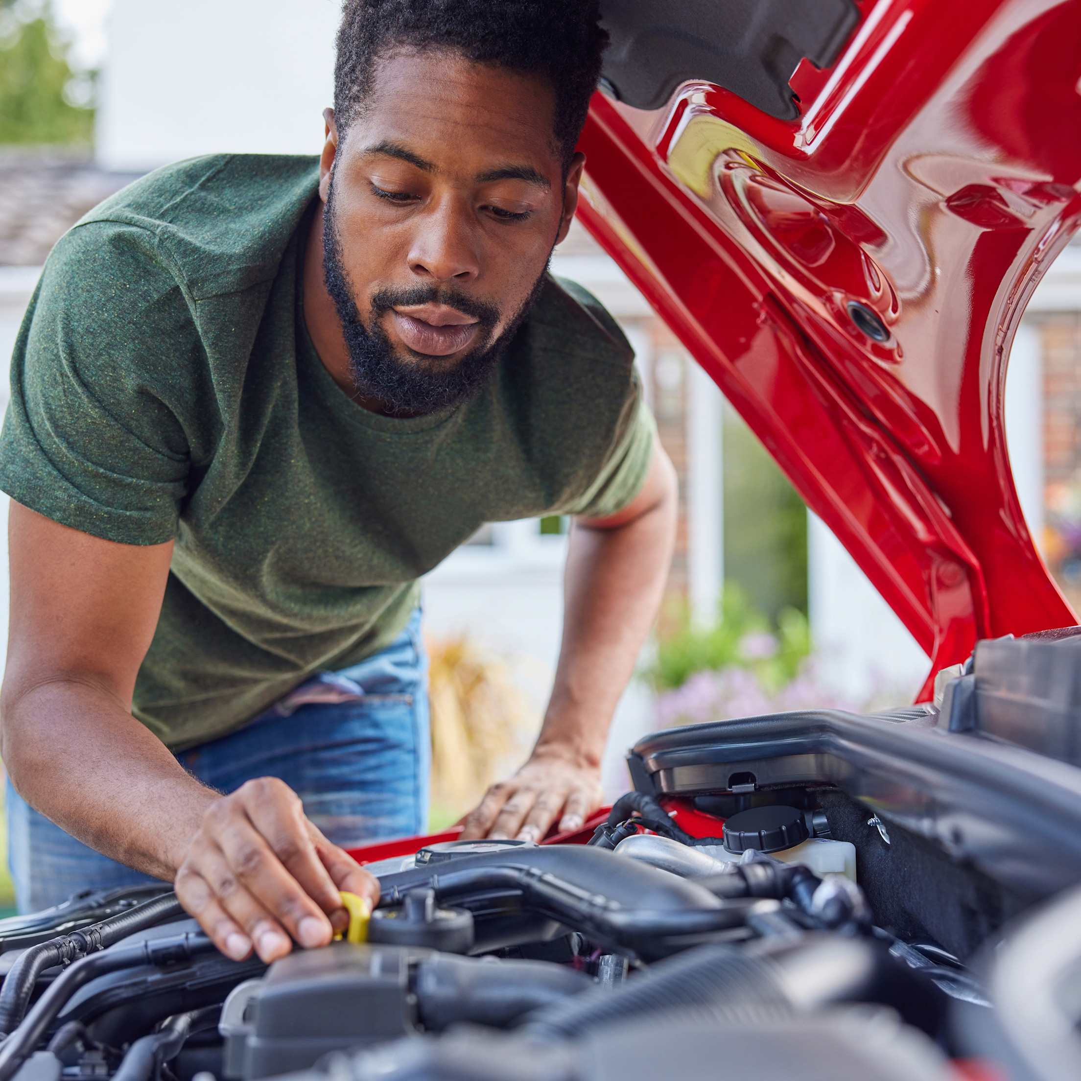 A person checks the engine oil on their red car.