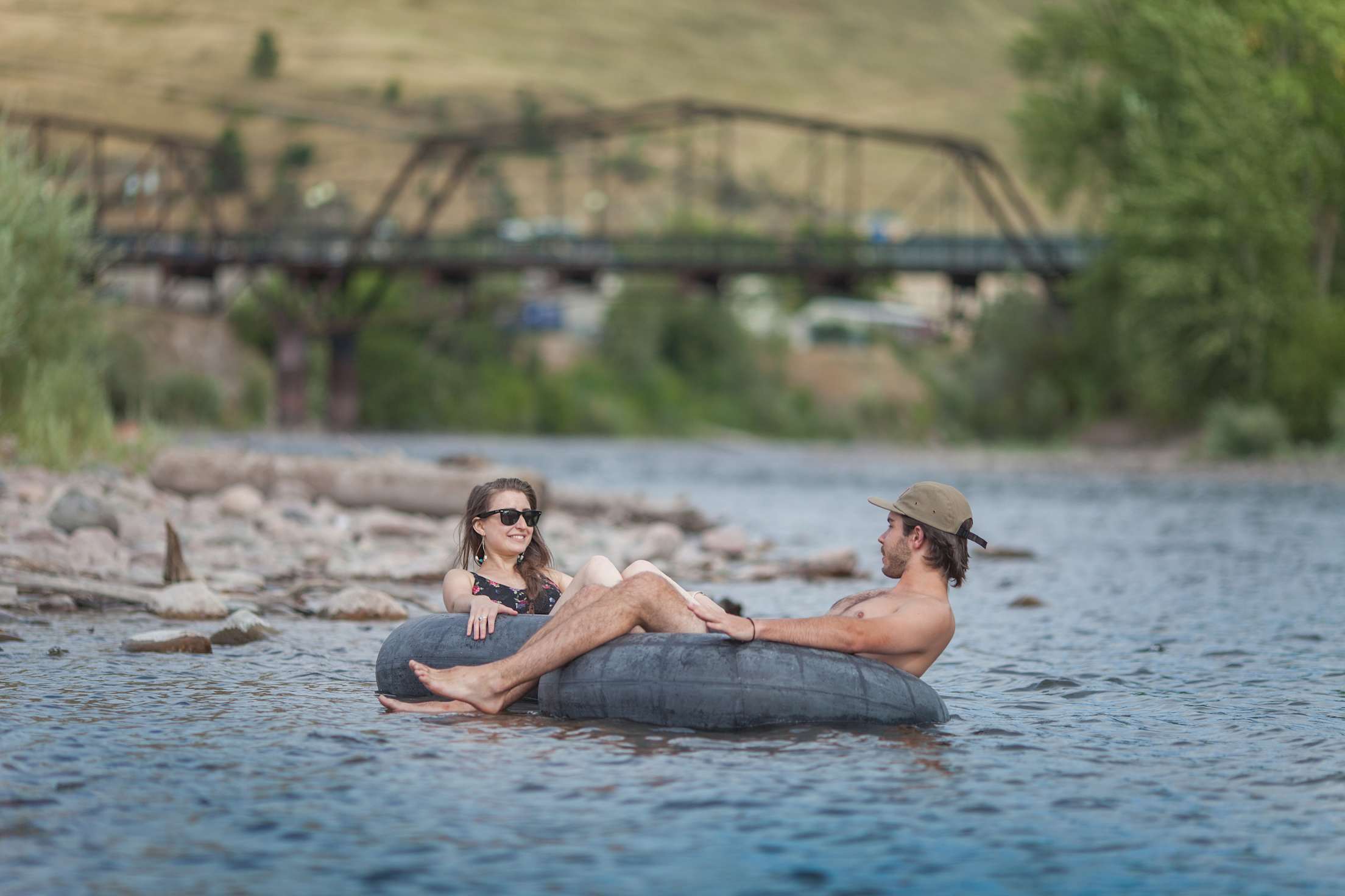 a woman and man float in inner tubes on a river with a bridge in the background