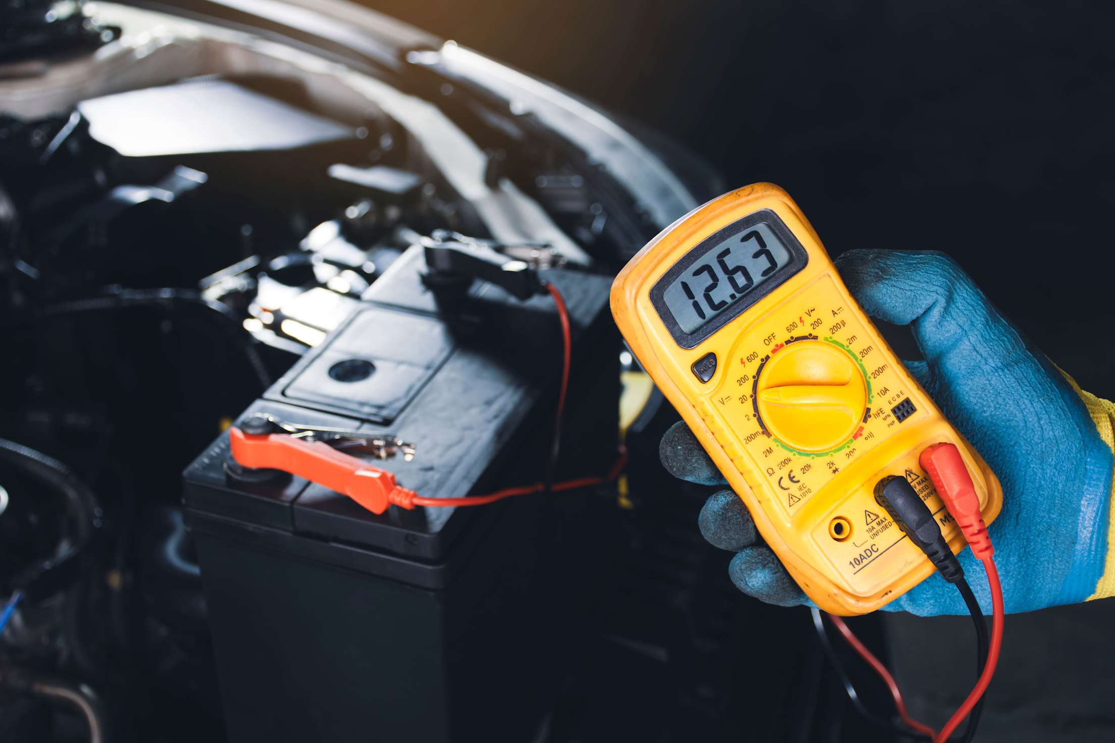 A mechanic tests the charge on a car battery with a multimeter.
