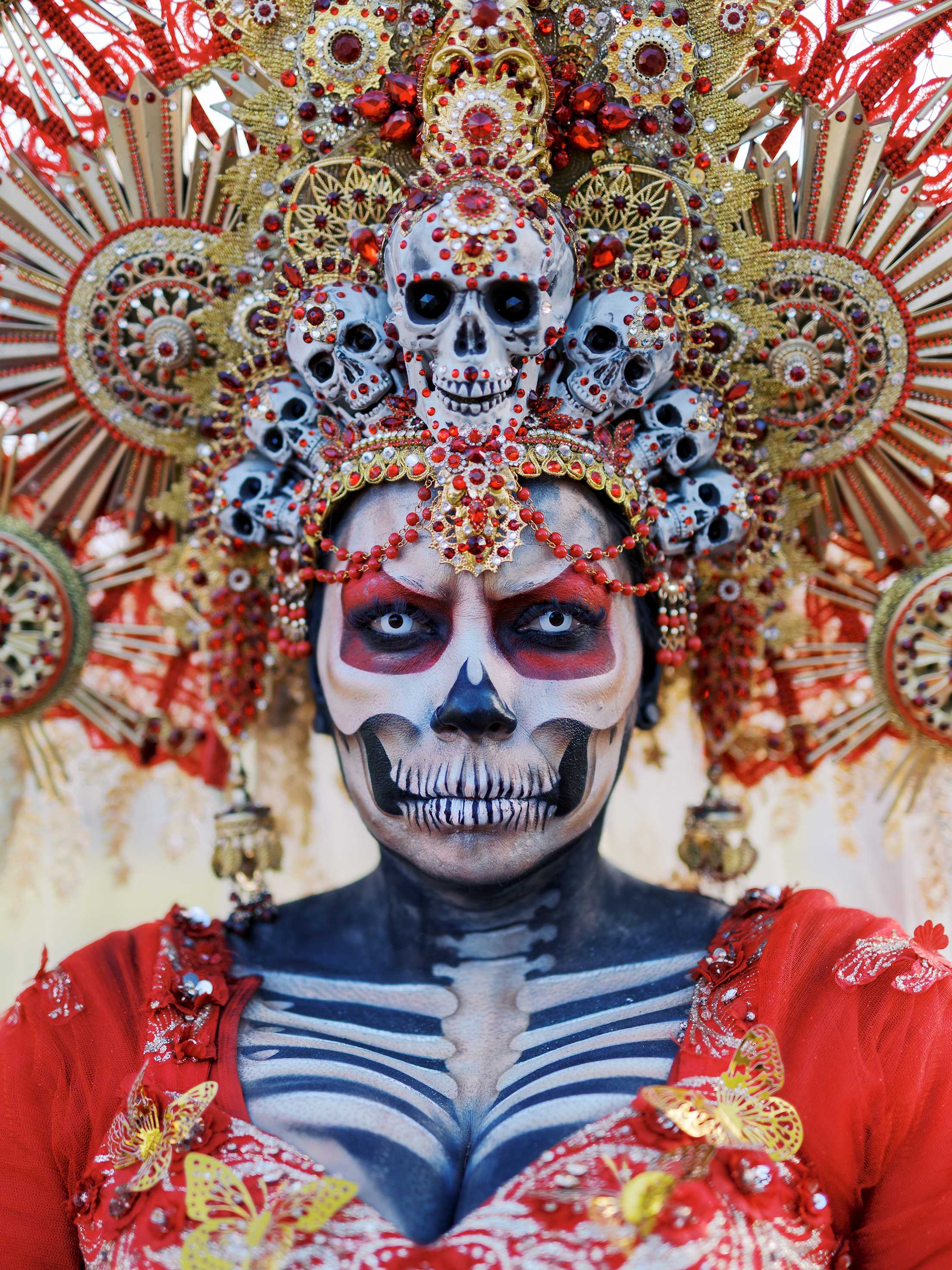 a person with elaborate skeleton makeup and a skeleton headdress in white red and gold