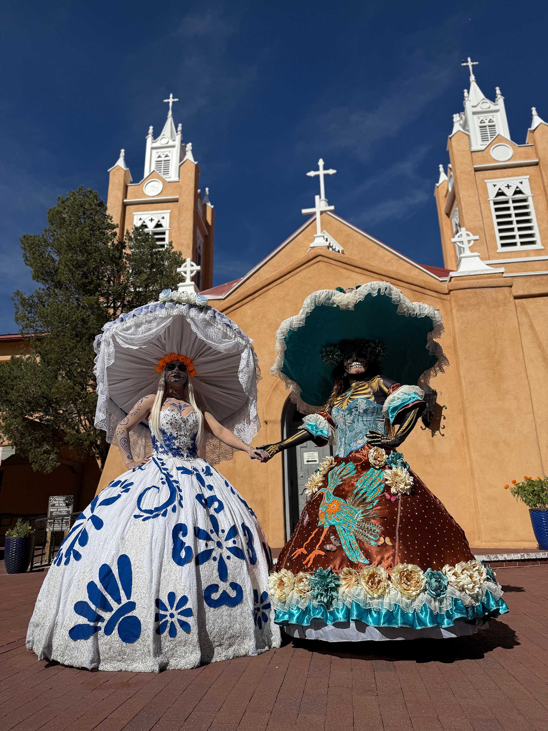 two women in elaborate day of the dead costumes and headdresses in front of a church