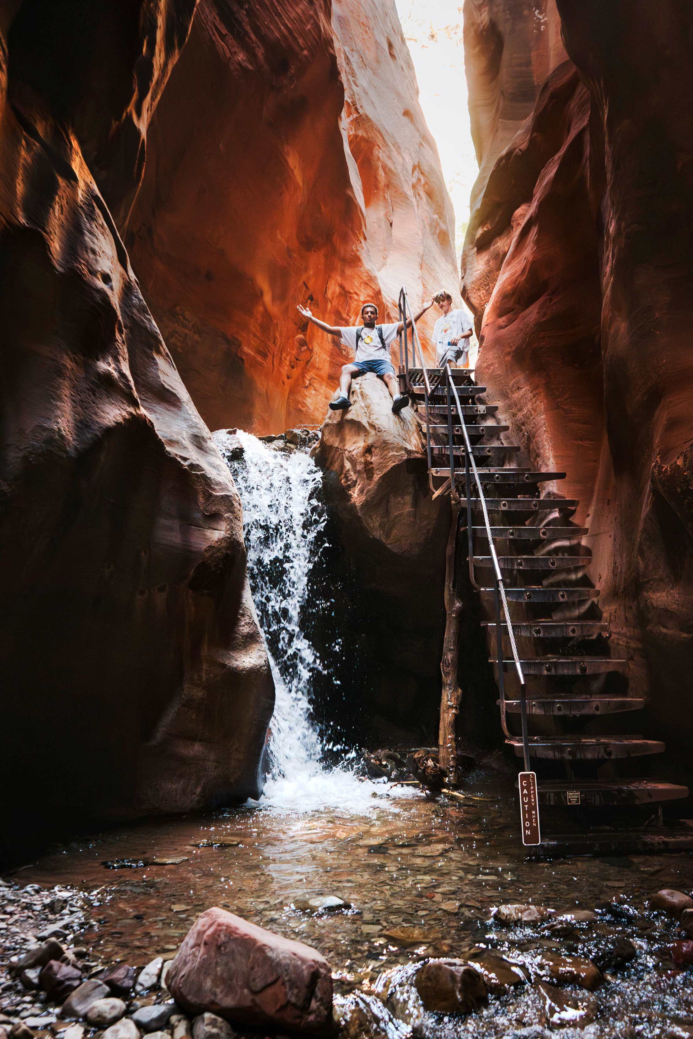 Two hikers atop the stairs next to Kanarra Falls in the slot canyon.