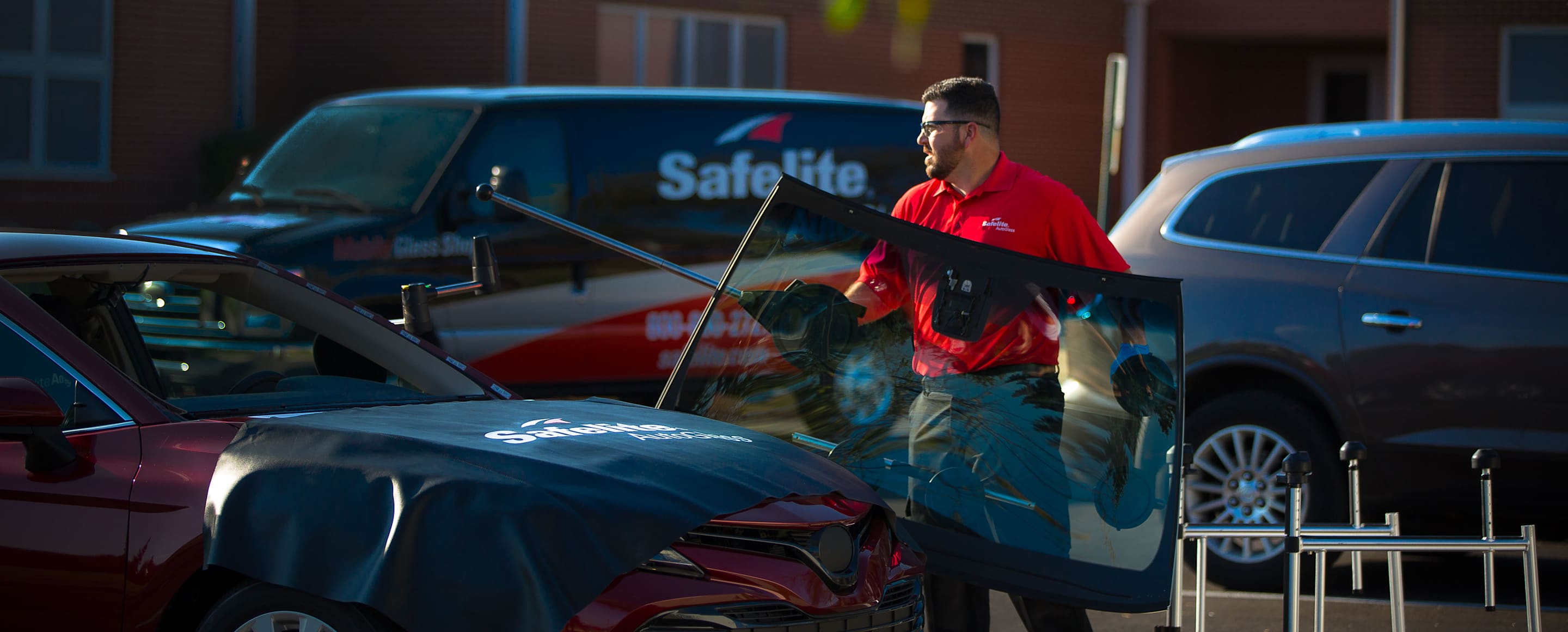 Safelite autoglass technician replacing a windshield with his van parked in the background