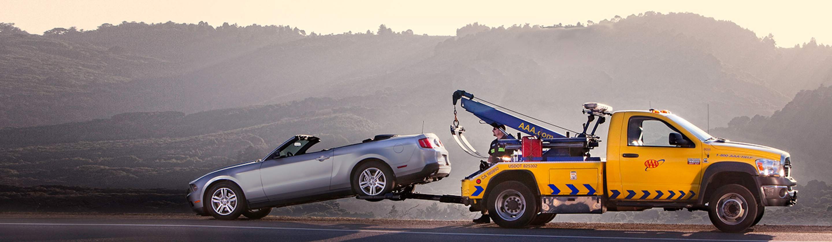 AAA yellow tow truck towing a silver convertible.