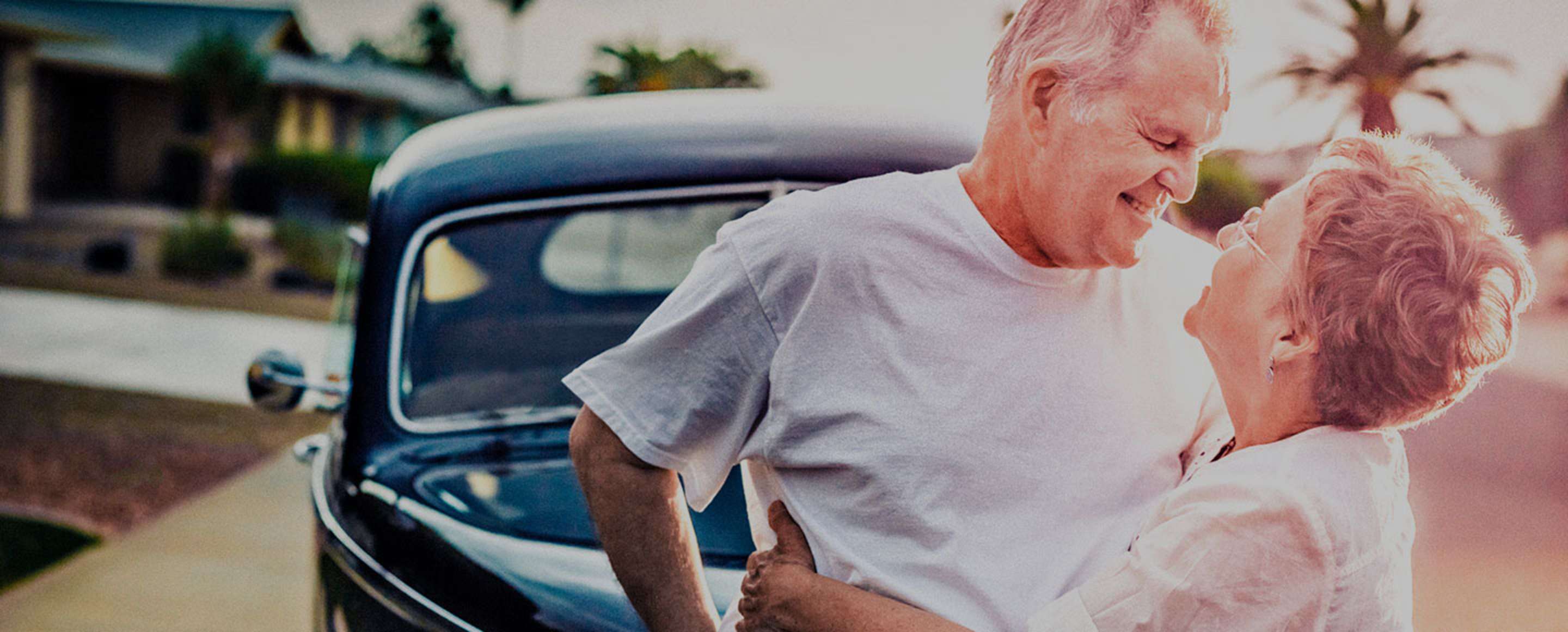 Two senior AAA Members embrace in front of a vintage car