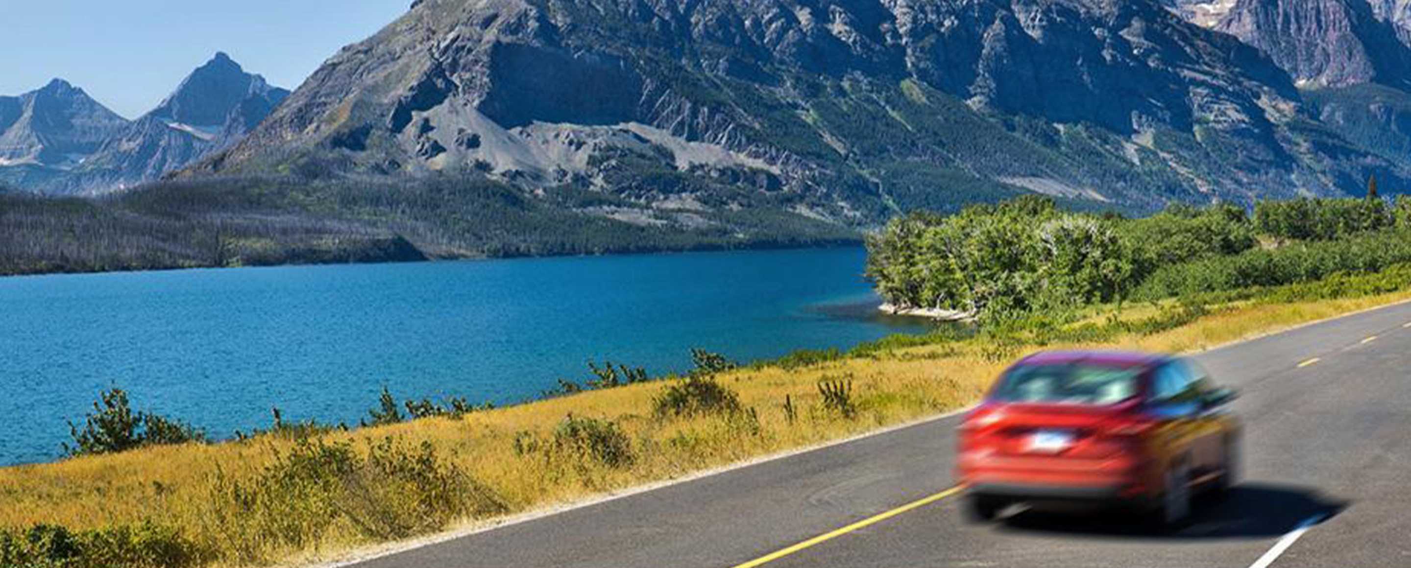 red car driving down a road by a lake