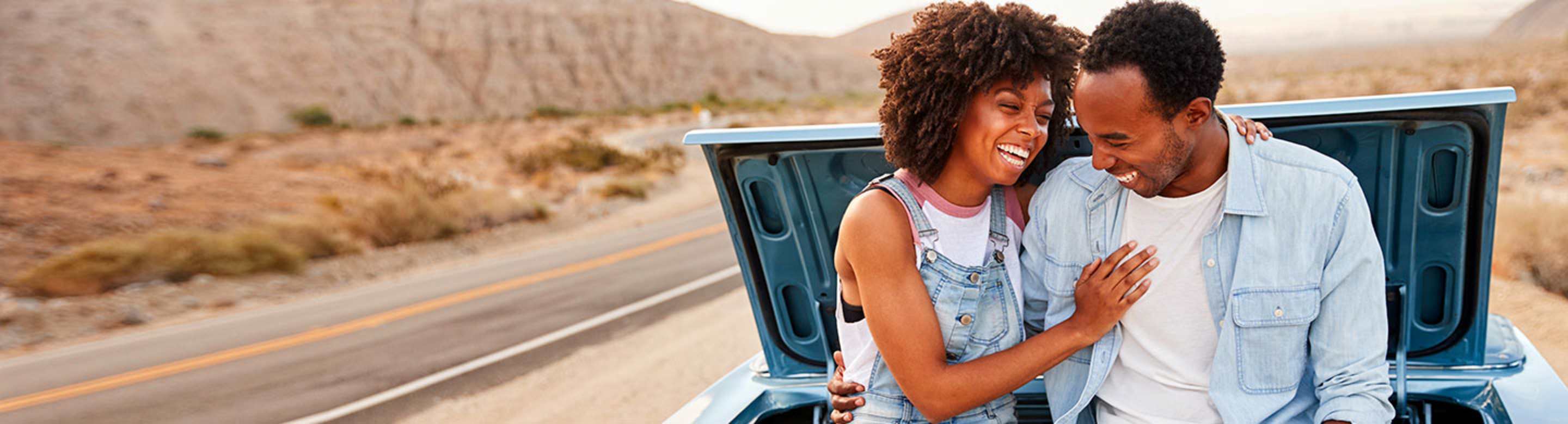 a couple sits on the back of their car while waiting for AAA roadside service