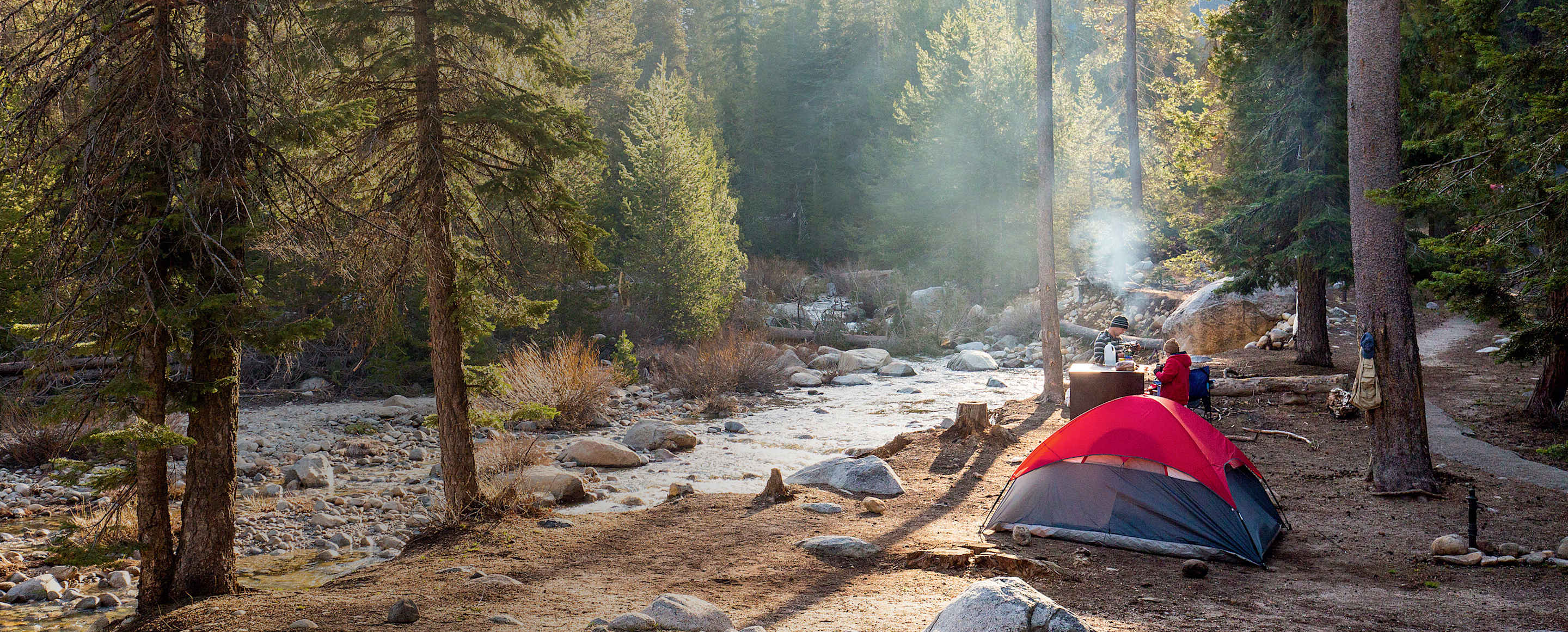 A couple cook at their campsite by a stream.