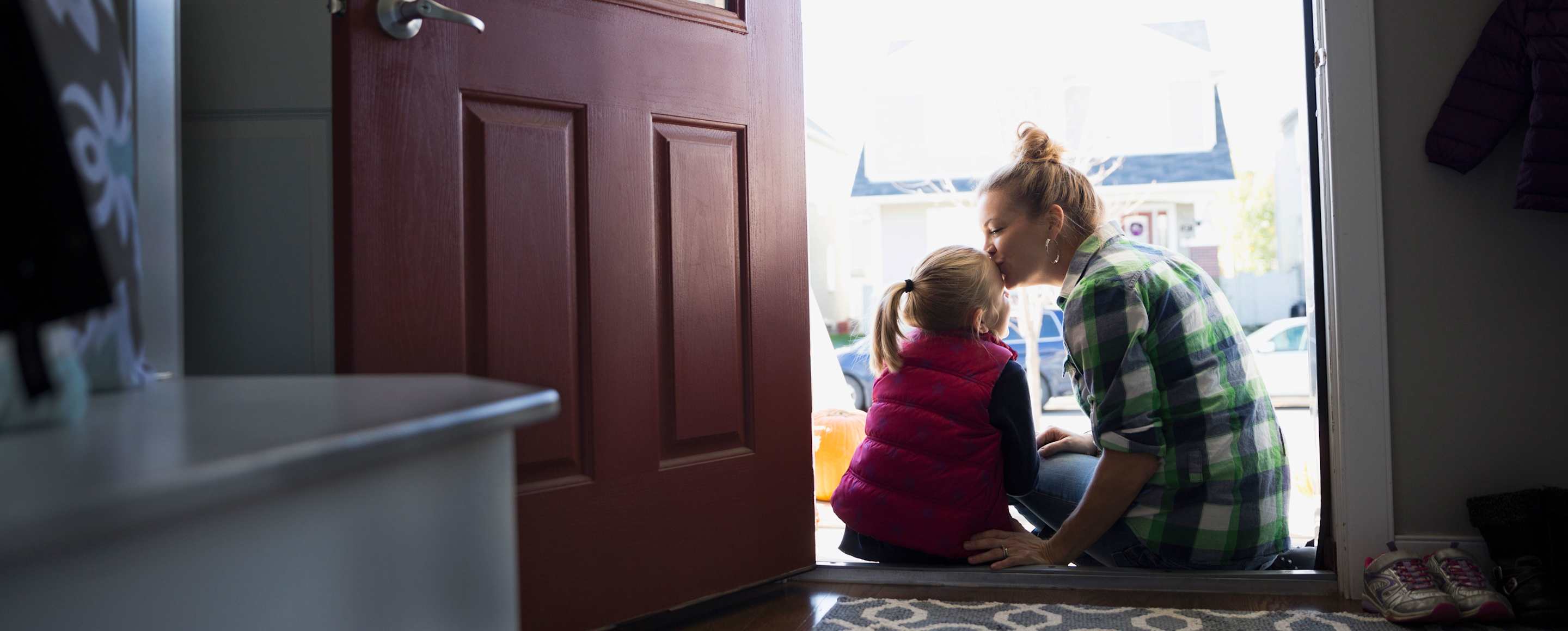 mother kissing her daughter on the head in the doorway of her home protected by AAA insurance.