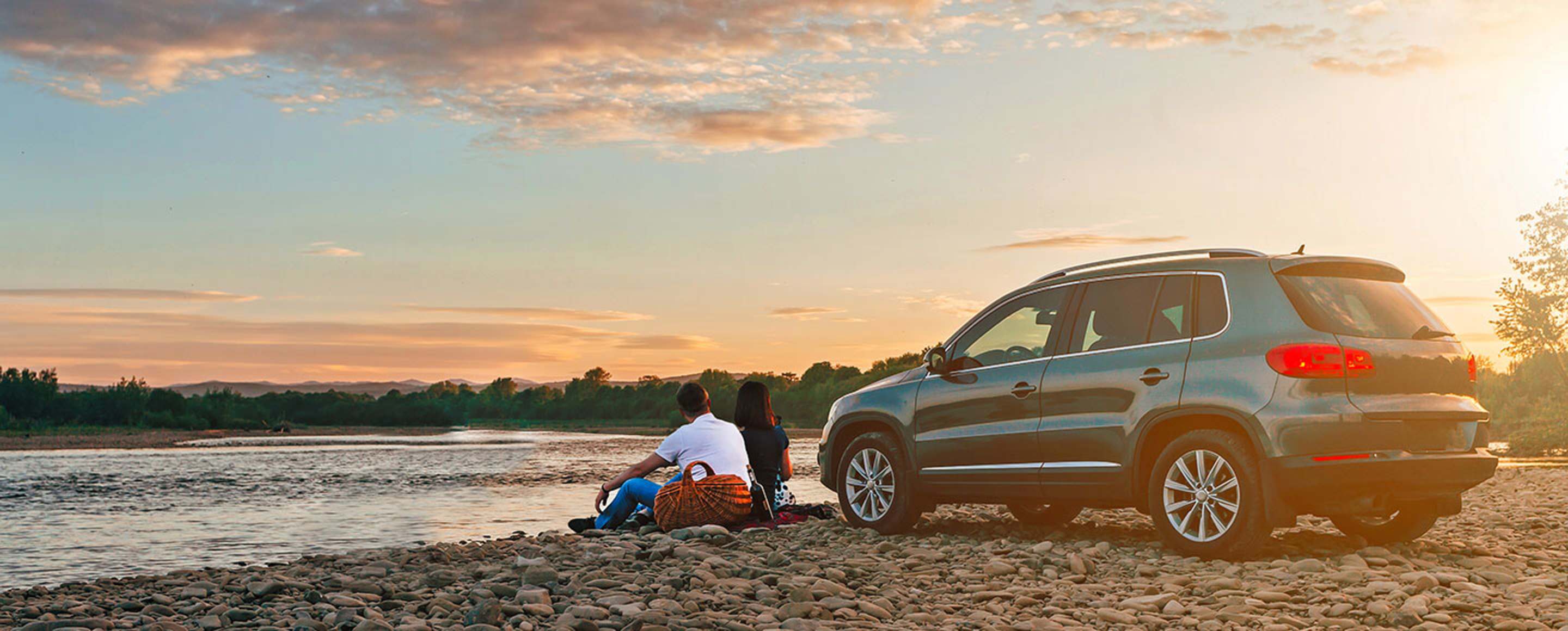 AAA members picnic next to their car on a rocky beach at sunset