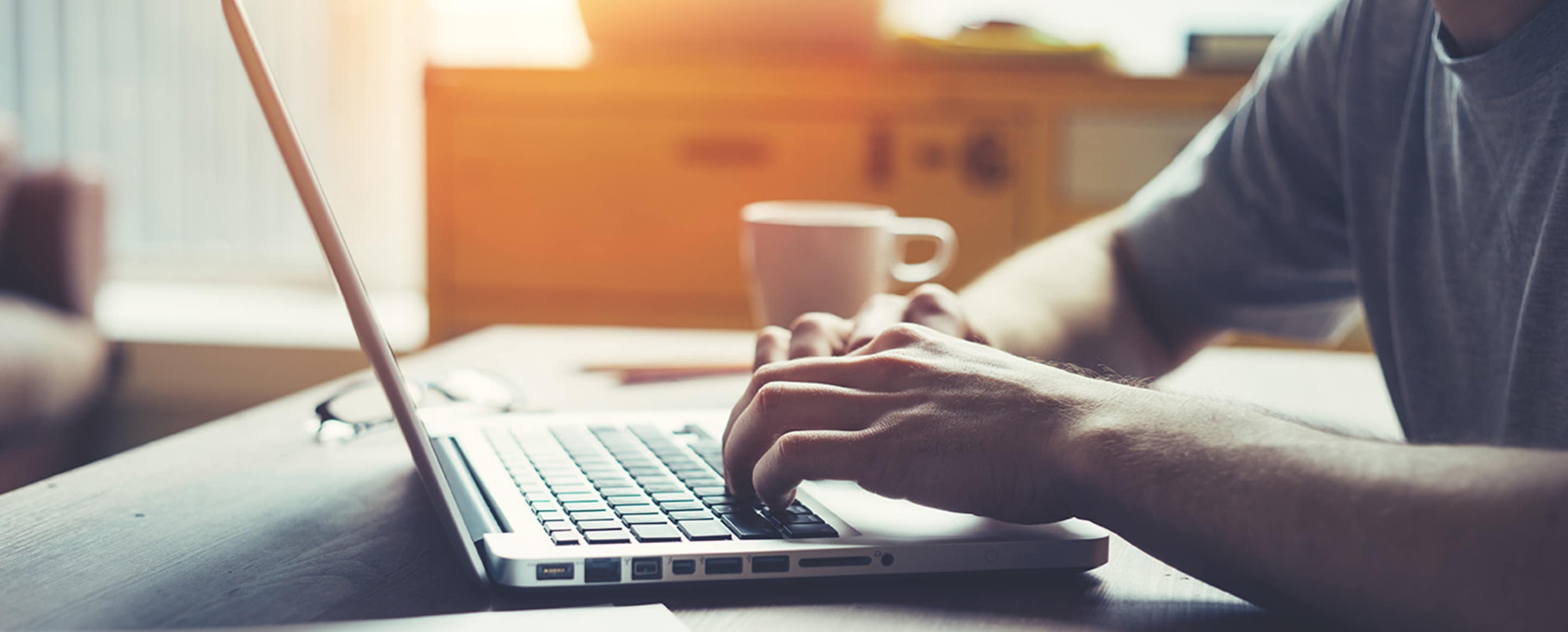 A writer with a cup of coffee types on a laptop