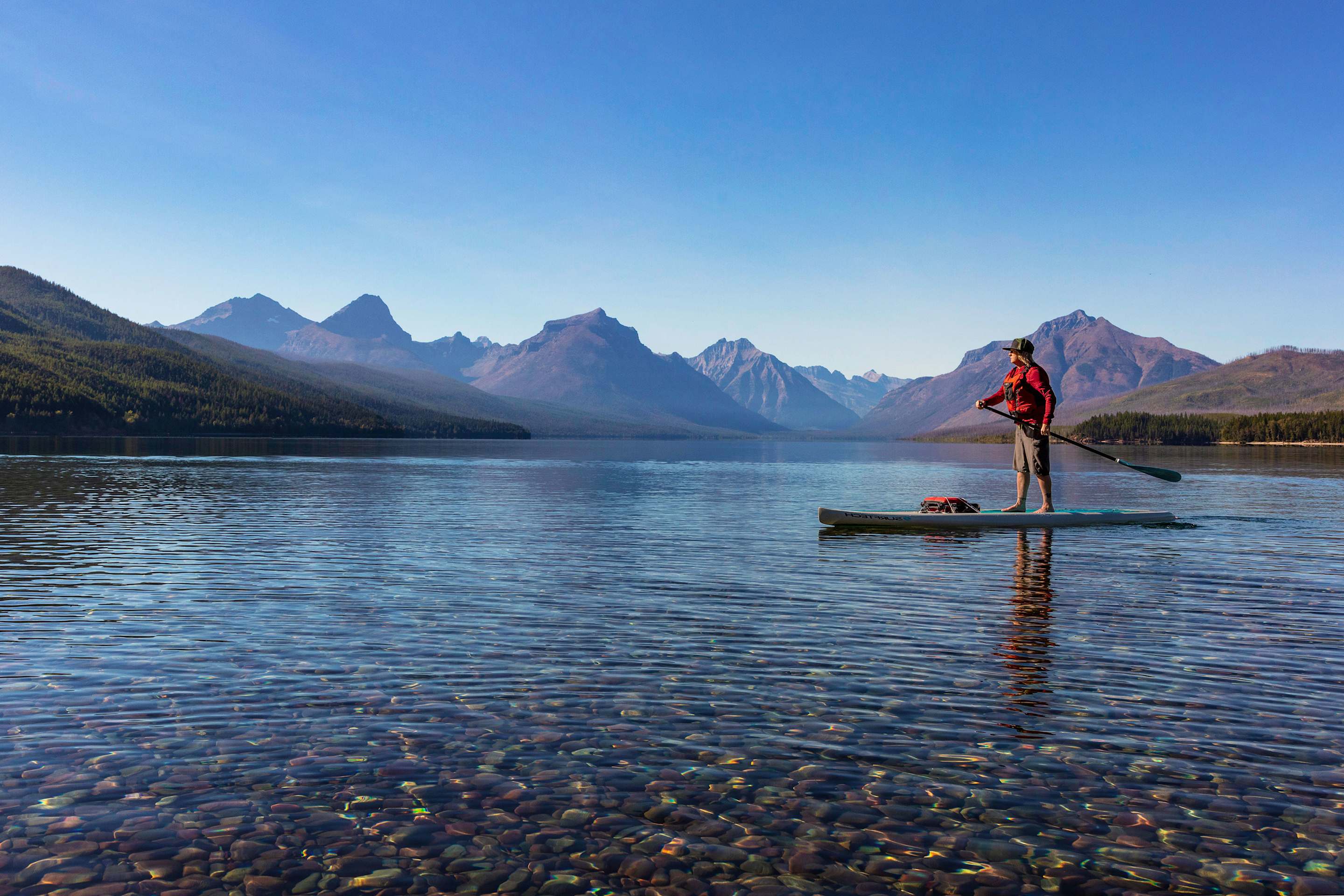A man standup paddleboards on Lake McDonald in Glacier National Park.
