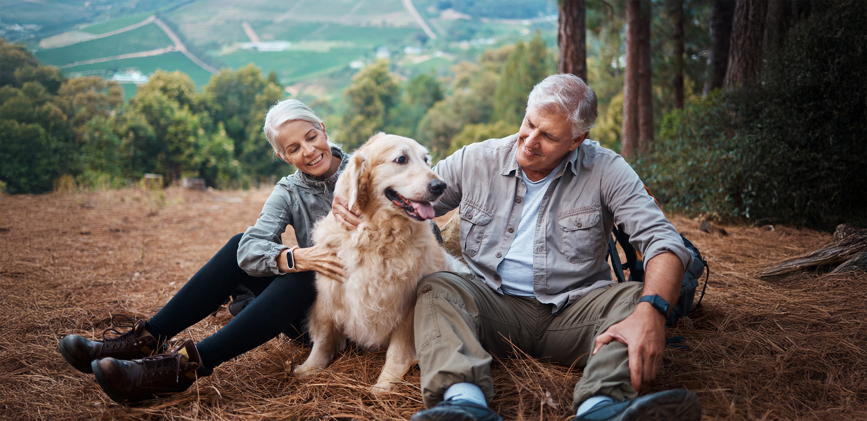 A couple pets their golden retriever, that's covered by AAA pet insurance, on a hiking trail