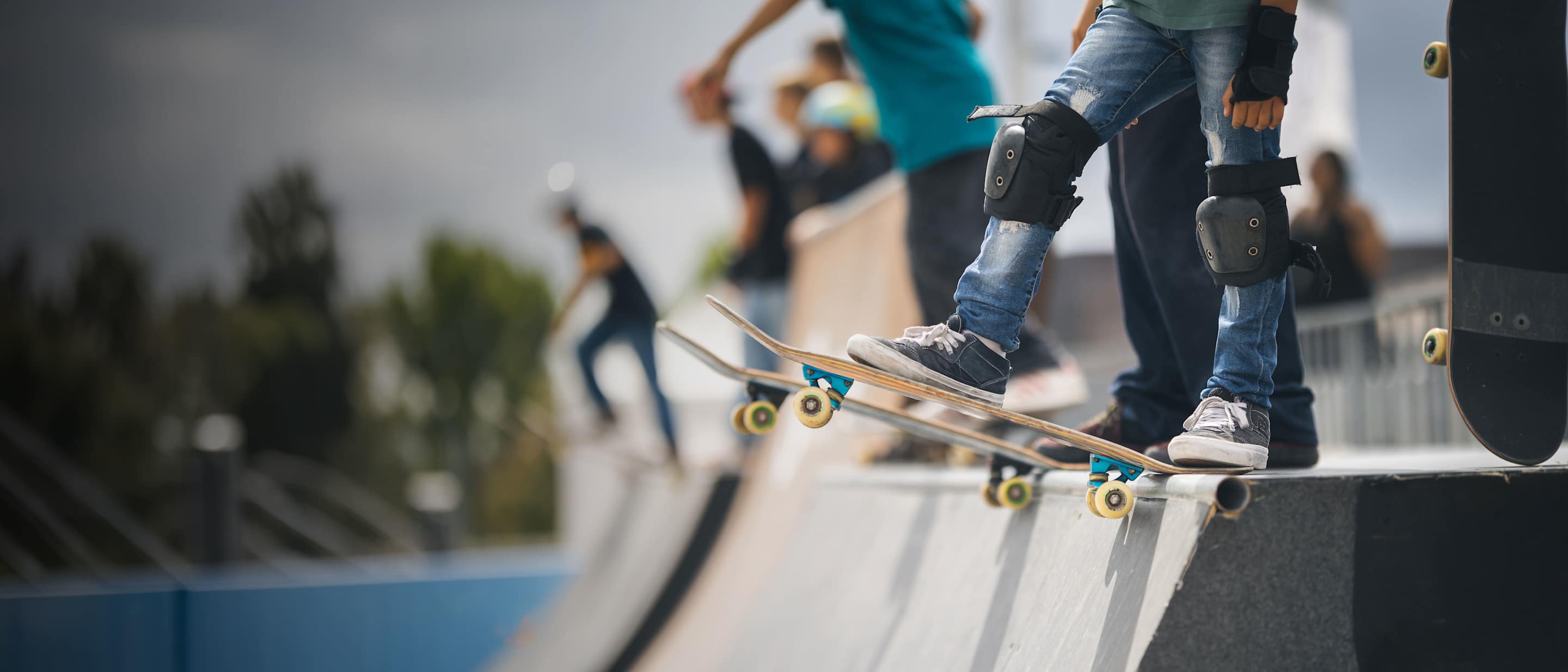 People wait on the endge of a half pipe with their skateboards.