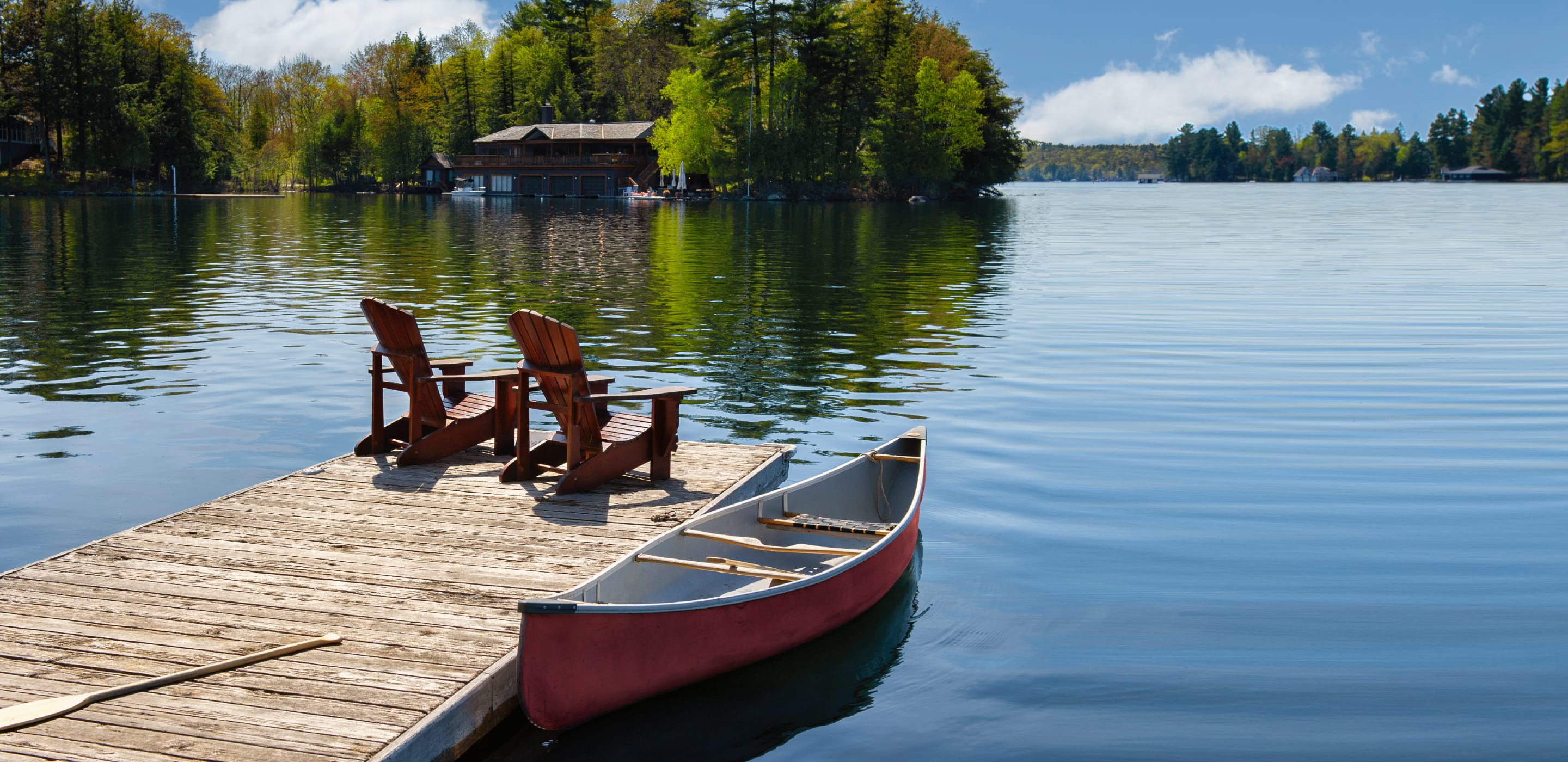 two chairs at the end of a doc on a lake