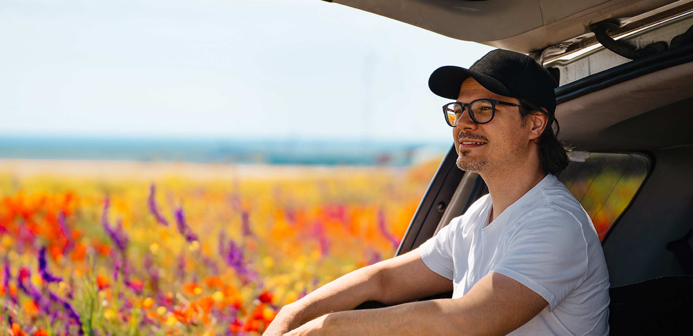 man sitting in the trunk of car in a field of flowers