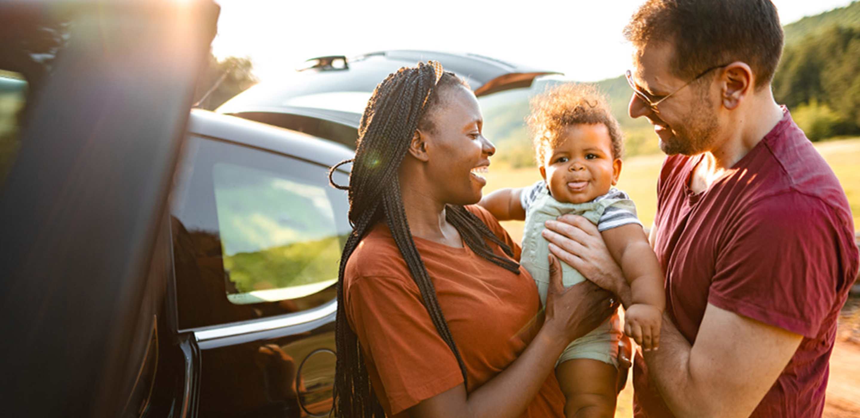 interracial couple with their baby standing outside their Hertz car rental