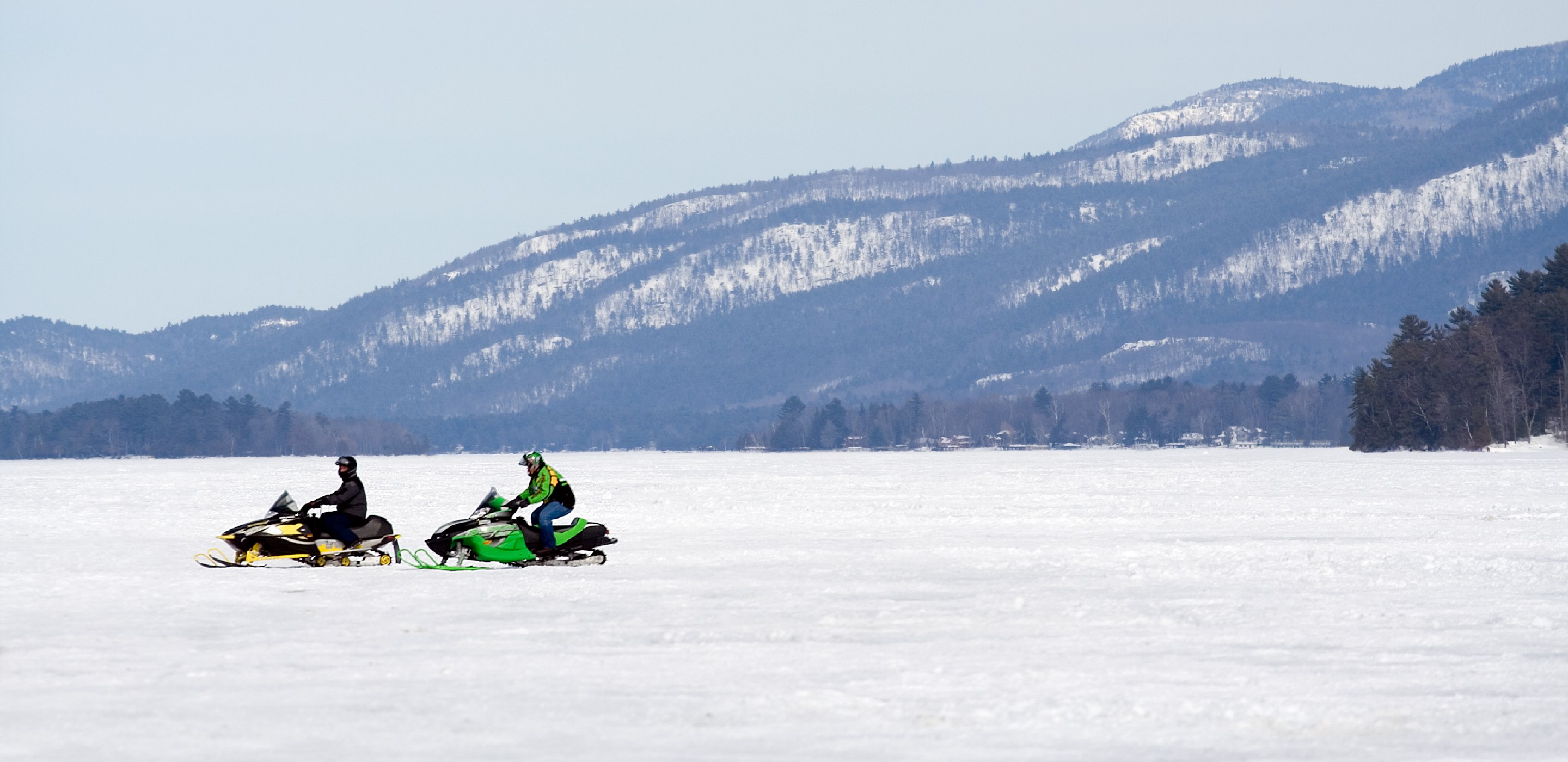 two drivers covered by AAA snowmobile insurance ride in a snowy mountain area