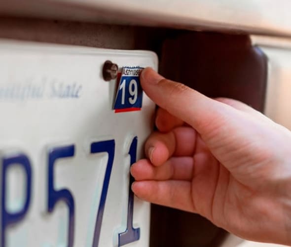 person affixes registration sticker to license plate