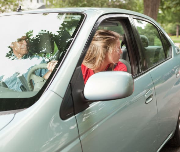 A teen practices reversing a car with her dad in the passenger seat.