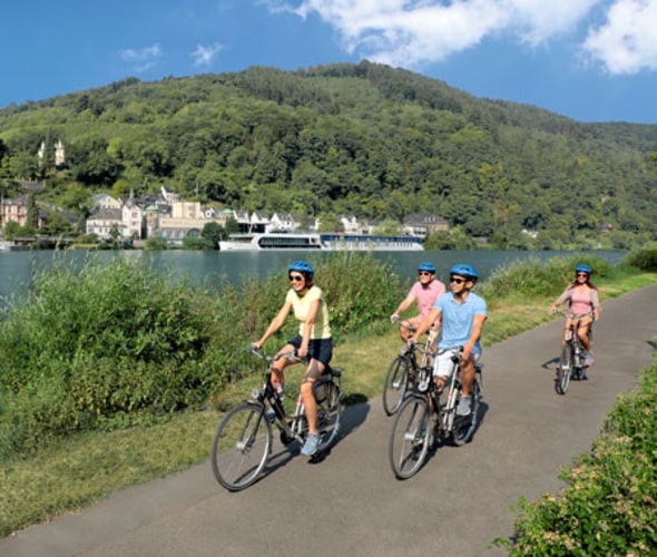 people riding bikes next to a river with an amawaterways ship in the background