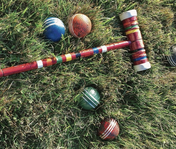 a red croquet mallet with a colorful croquet balls lying on grass