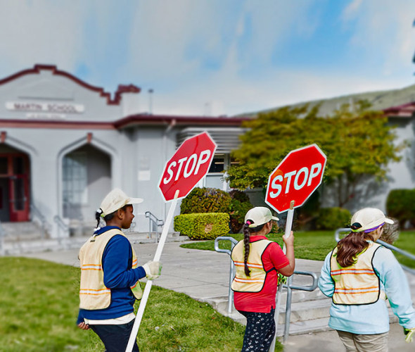  AAA School Safety Patrol students walking in a line in front of their school holding stop signs.