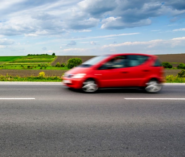 Small red car with AAA auto insurance coverage driving on a country road