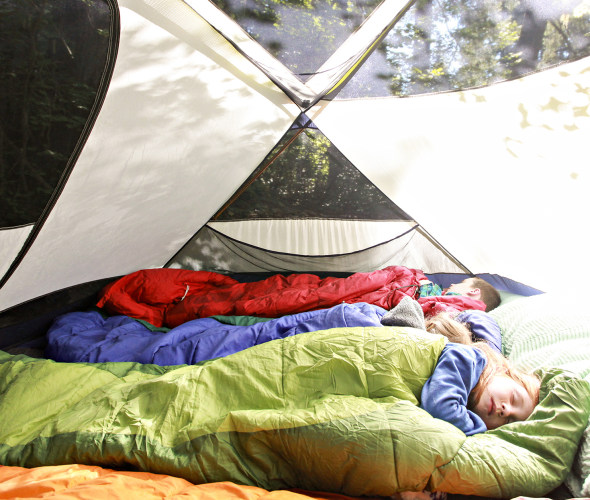 Children sleep in sleeping bags inside a bright tent.