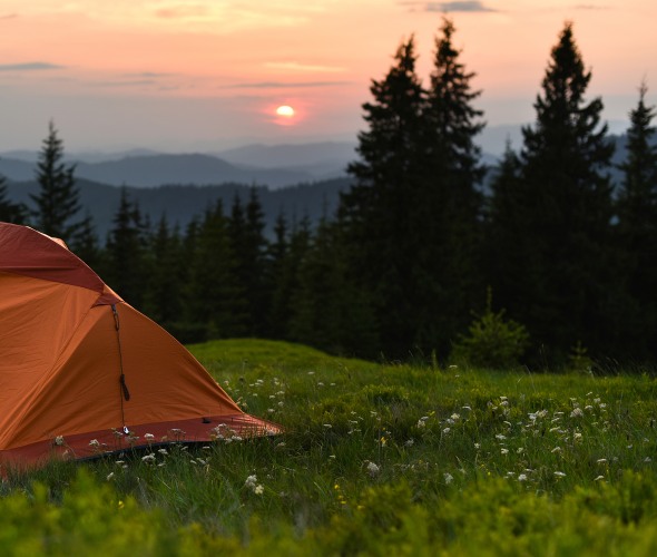tent on a hill overlooking mountains at sunset.