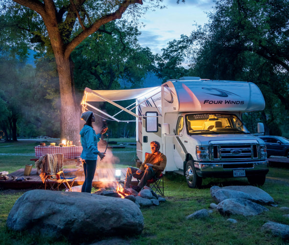 A couple relax around a campfire outside their RV.