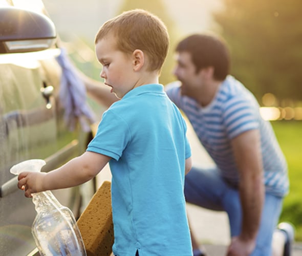 a son and kneeling father wash a car together