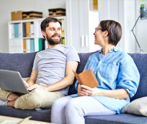 couple laughing while sitting on a blue sofa in their home covered by AAA homeowners insurance