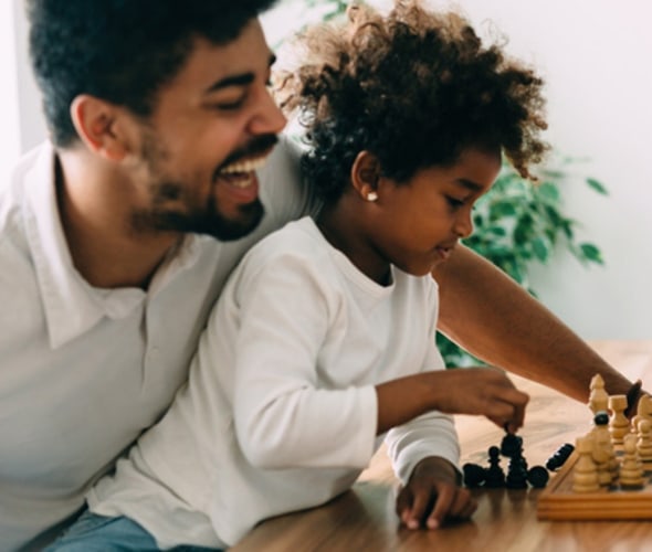 father laughing while teaching daughter to play chess in their home protected by AAA homeowners insurance