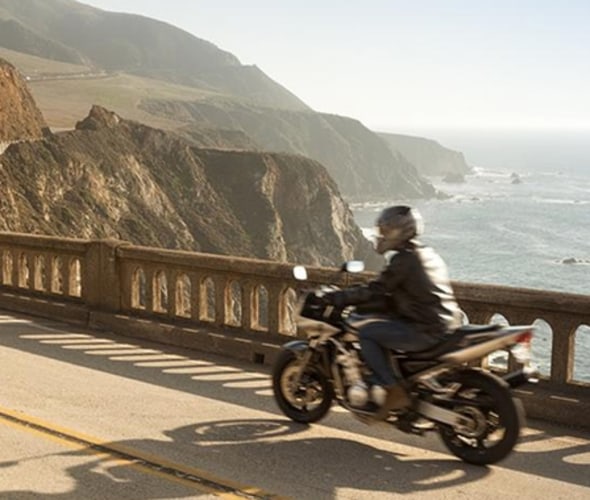 aaa member riding a motorcycle over a bridge with cliffs in the distance