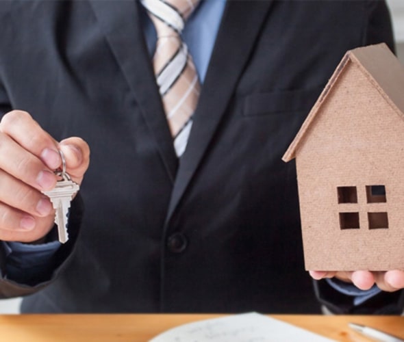 Man in a business suit holding out the keys to a new home