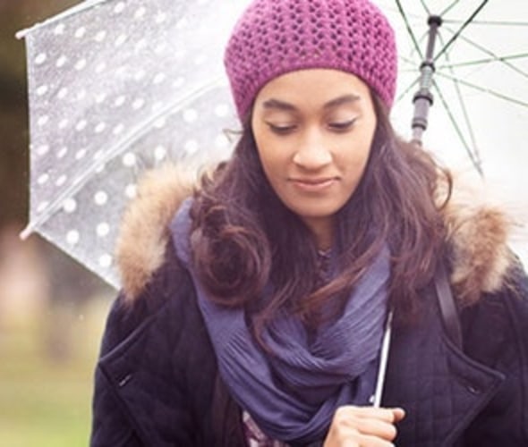 A woman with AAA personal umbrella protection insurance stands under an umbrella in the rain