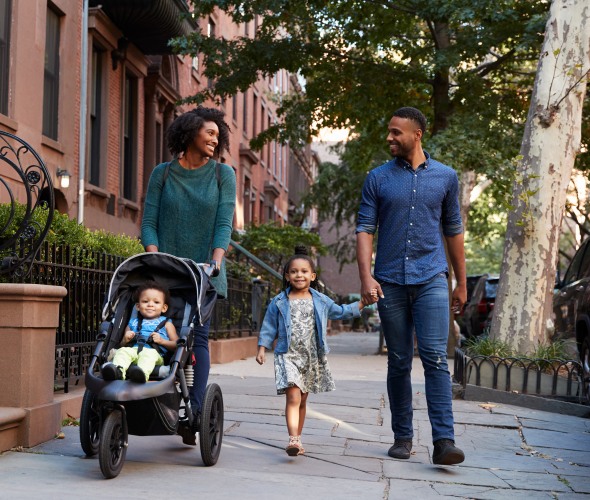 Family walks down a street in New York with a young girl and a baby in a stroller.
