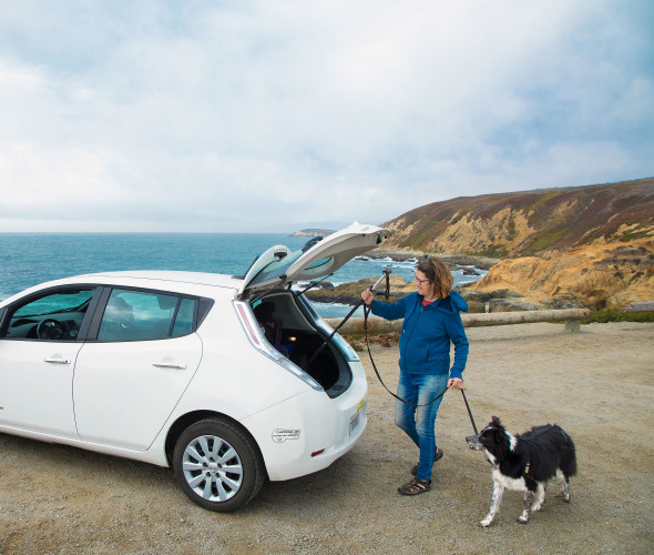 A woman loads hiking poles into the back of her Nissan Leaf EV.