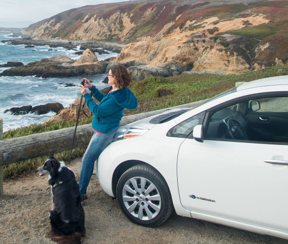 A woman overlooks the Pacifica Ocean alongside her dog and her Nissan Leaf.